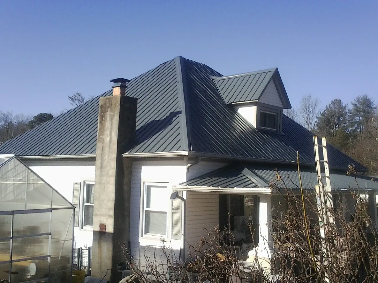 Dark blue standing seam metal roof on a white farmhouse with dormer — Slate & Tile Roof Repair by Roofing Brothers in Bend