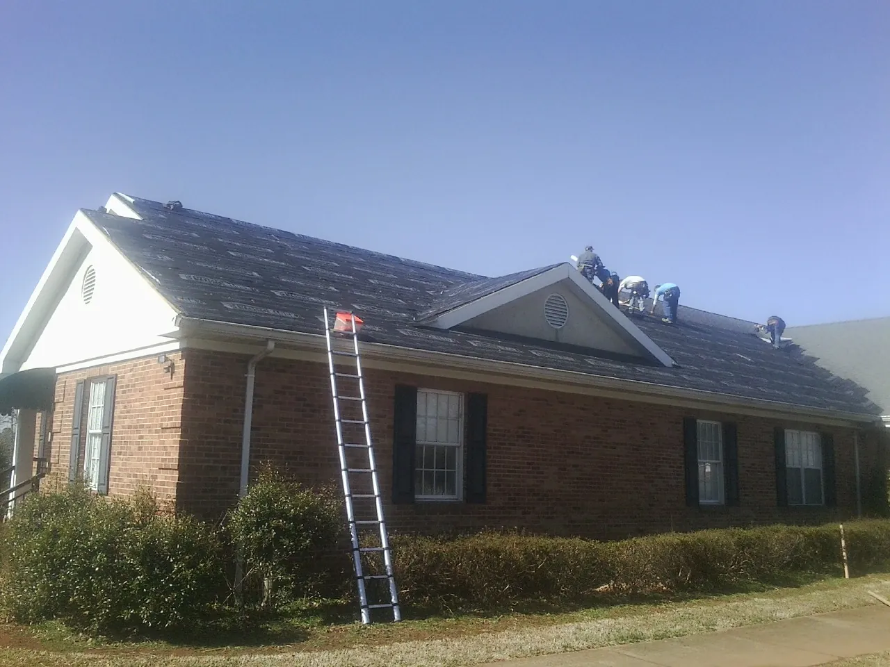 Crew tearing shingles off a brick ranch roof with a ladder set — Metal Roof Repair work by our crew in Bend