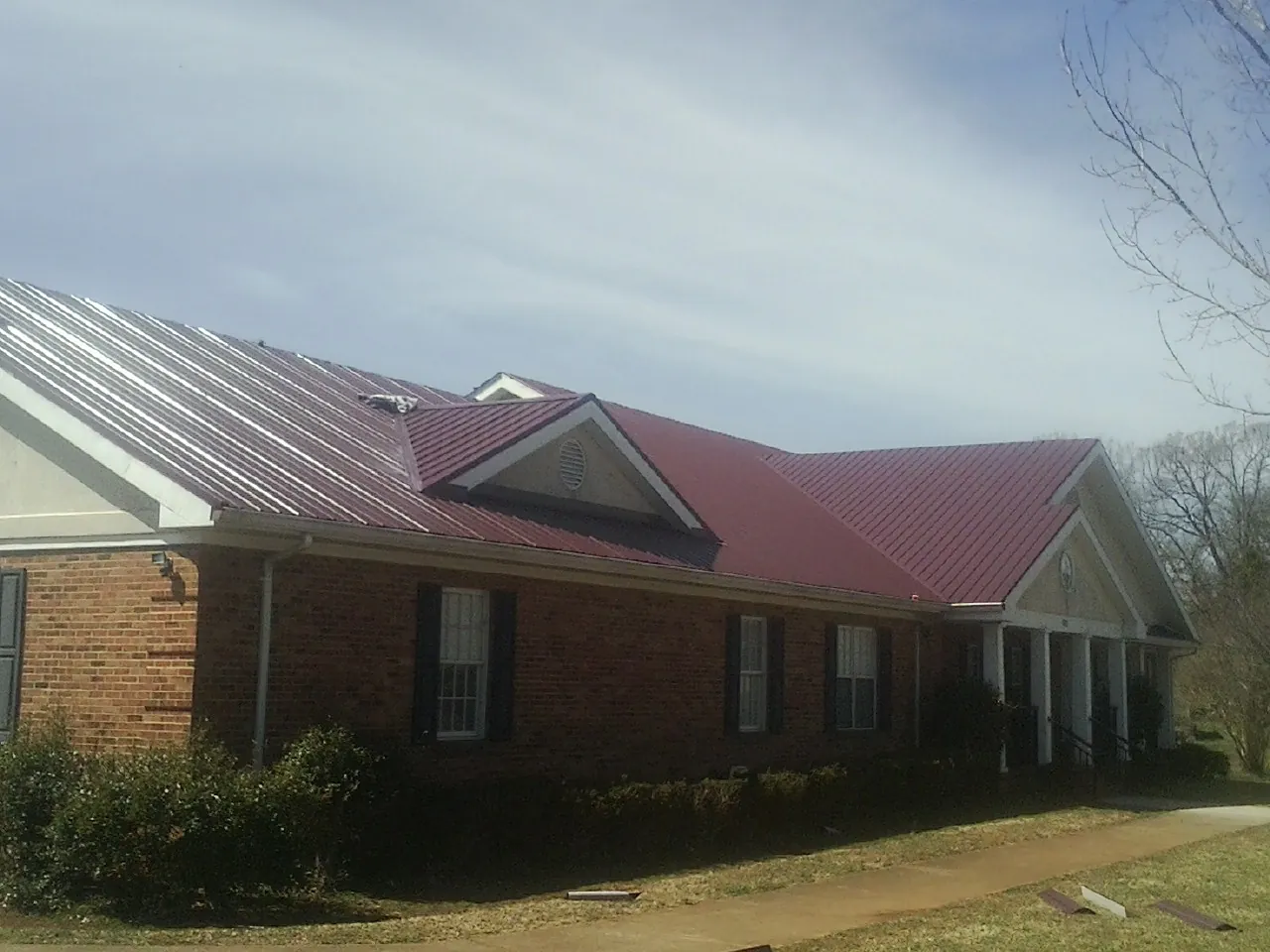 Red metal roof with gabled entries on a long brick building, from a Hail Damage Roof Repair job in Bend