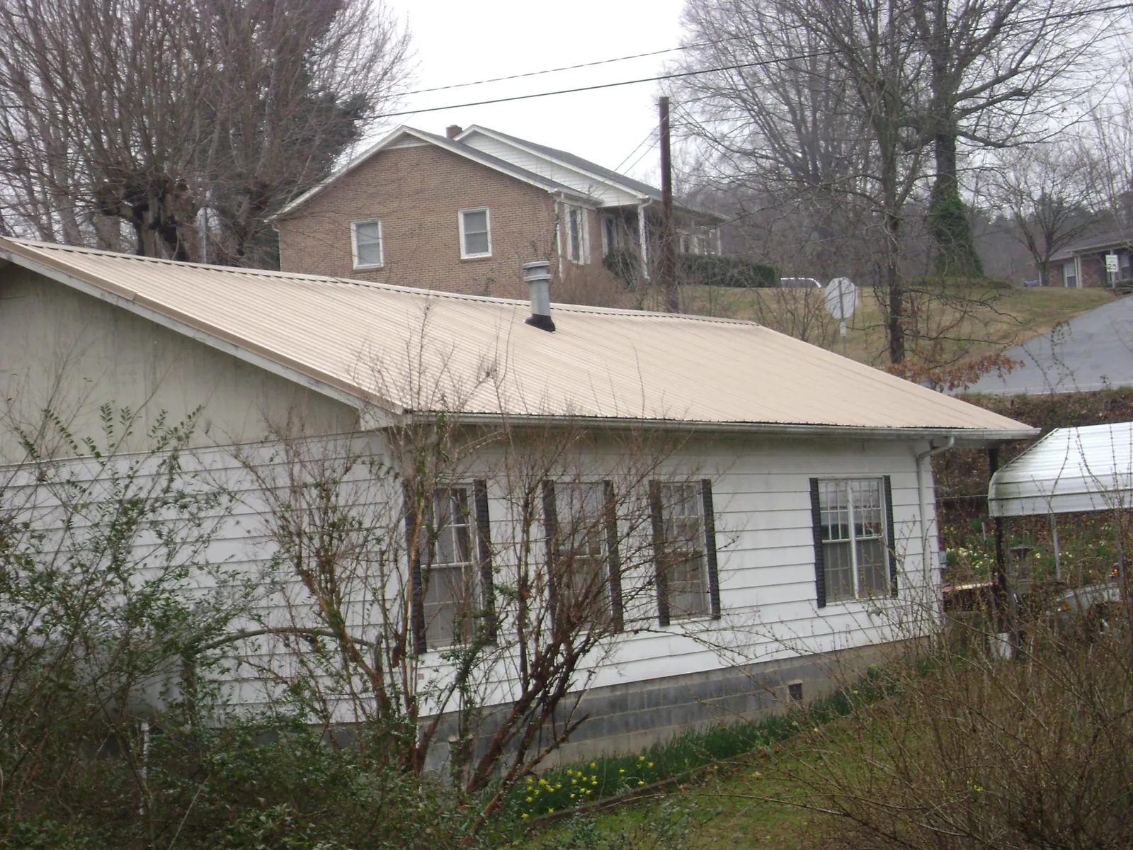 Tan metal roof on a white sided house set into a hillside — Commercial Roofing by Roofing Brothers in Bend